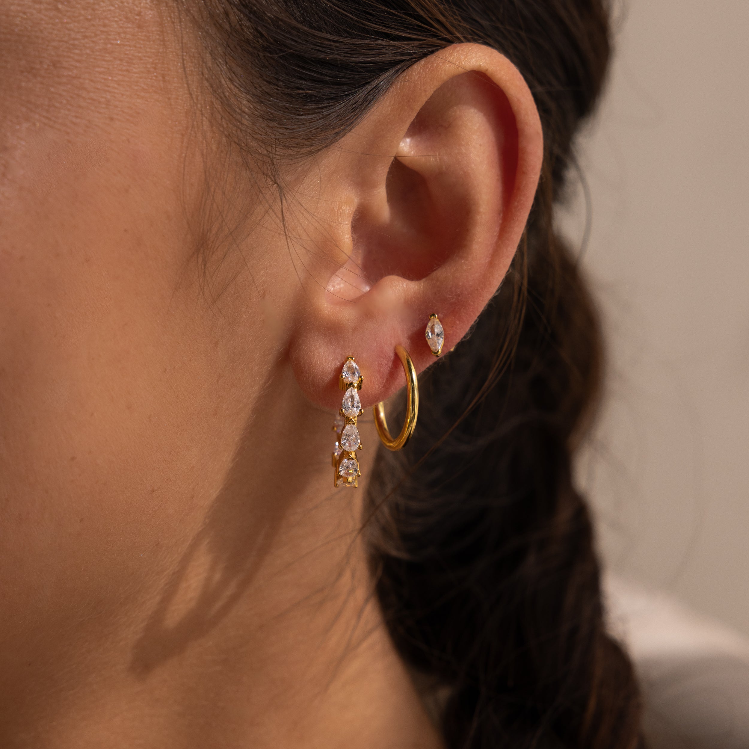 Close-up of a womans ear adorned with multiple gold and gemstone earrings, featuring statement hoops and sparkling Inside Out Pear Diamond Hoops.