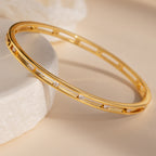 Lace Diamond Bangle in 18K Gold with small round diamonds and an open station design, shown on a light beige surface and white stone.