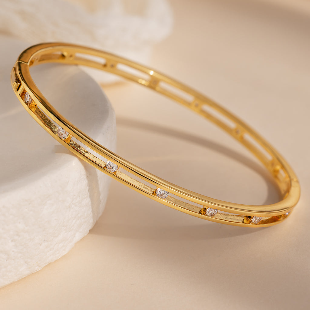 The Lace Diamond Bangle, featuring delicate gold and sparkling diamonds, is elegantly displayed on a light surface with soft, neutral lighting—a striking luxury jewelry piece.