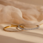 Side-by-side display of the Marquise Diamond Tennis Bracelet in silver and gold, both sparkling with marquise-cut diamonds, resting on soft fabric.