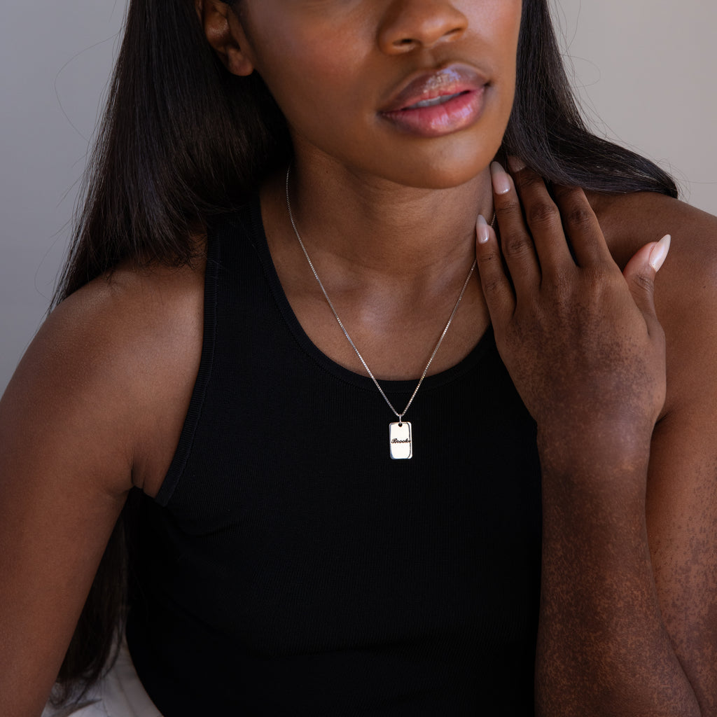 Woman wearing the Name Tag Necklace in Sterling Silver with a black tank top, her hand resting on her collarbone against a neutral background.