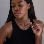 A woman in a black tank top wears the Inner Circle Necklace, looking down and thoughtfully holding its pendant.