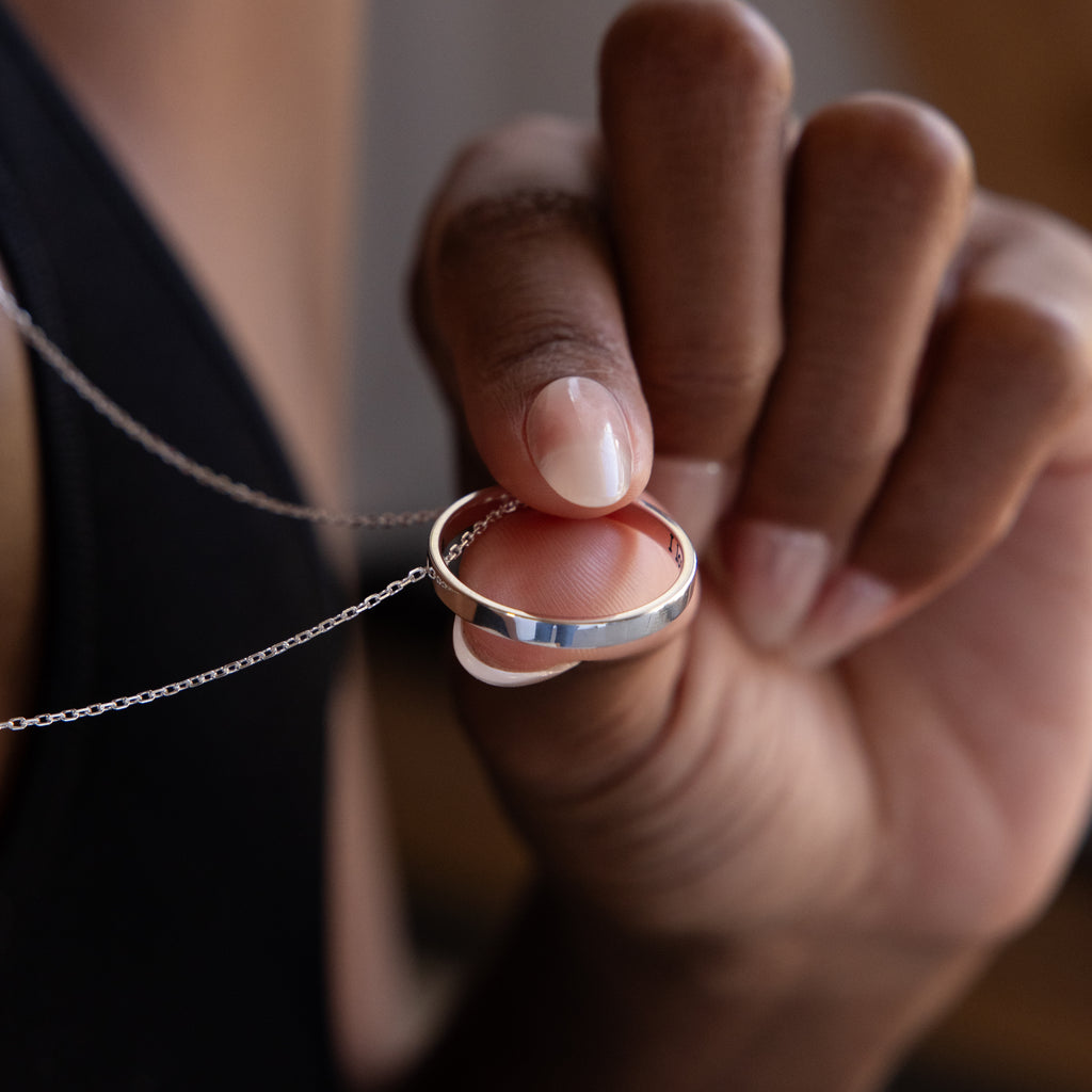 A hand holds the Inner Circle Necklace in Sterling Silver, featuring a sleek ring pendant gracefully suspended on a fine chain.