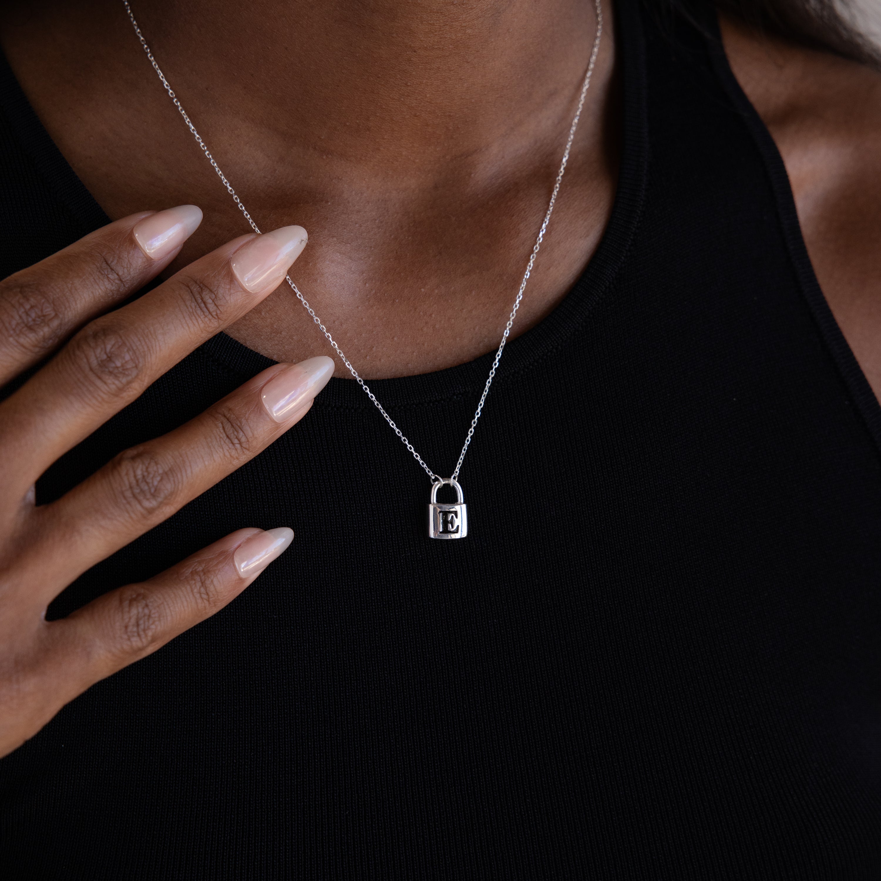 A person makes a bold fashion statement with the Padlock Necklace in Sterling Silver, featuring the letter E, paired with a sleek black top.
