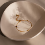 Heart Station Bracelet in 18K Gold, featuring delicate heart charms, is a romantic stacking piece shown on a textured off-white ceramic dish under soft light.