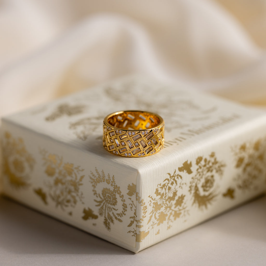 The Mosaic Diamond Baguette Ring, featuring an intricate geometric design, rests on a decorative cream and gold floral box.