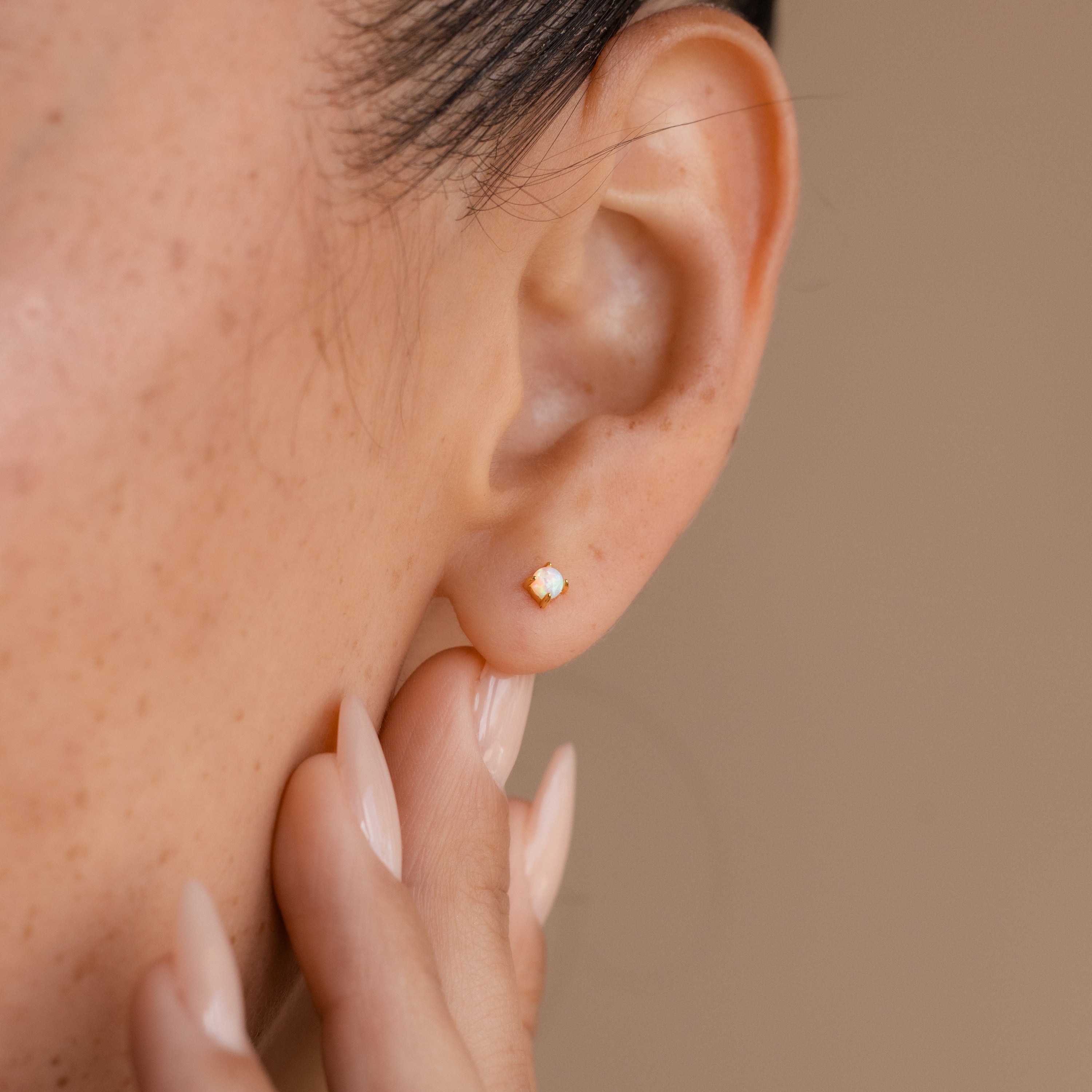 Close-up of a person wearing the dainty Opal Flat Back Studs and touching their ear with manicured fingers.
