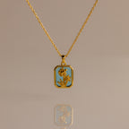 Blue Zircon Birth Flower Charm Necklace with a rectangular blue pendant featuring a floral design, displayed on a neutral background.