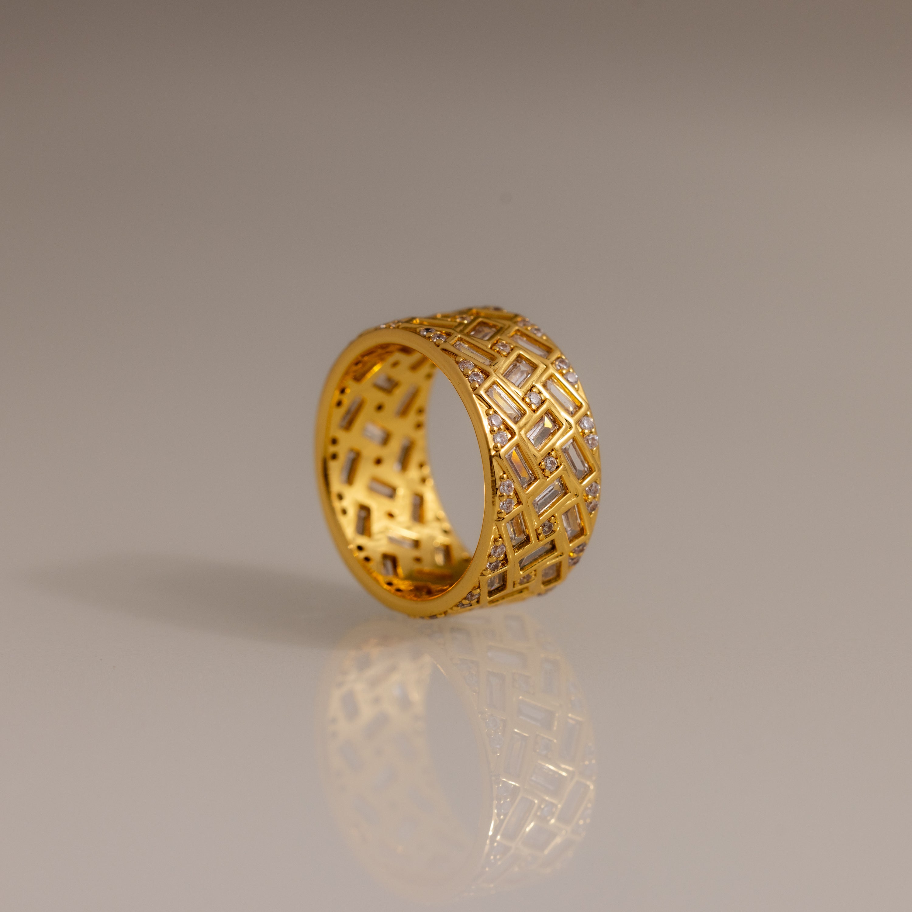 Bold and eye-catching, the Mosaic Diamond Baguette Ring features a wide gold band with a geometric lattice pattern and small embedded diamonds set against a plain background.