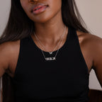 A woman in a black tank top wears two silver necklaces: a Pave Initial Necklace in Sterling Silver with an M and another spelling CECILIA.