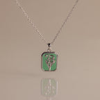 Silver necklace with a rectangular green emerald birth flower charm displayed on a reflective surface—I'm sorry, but there is no product description provided for further details.