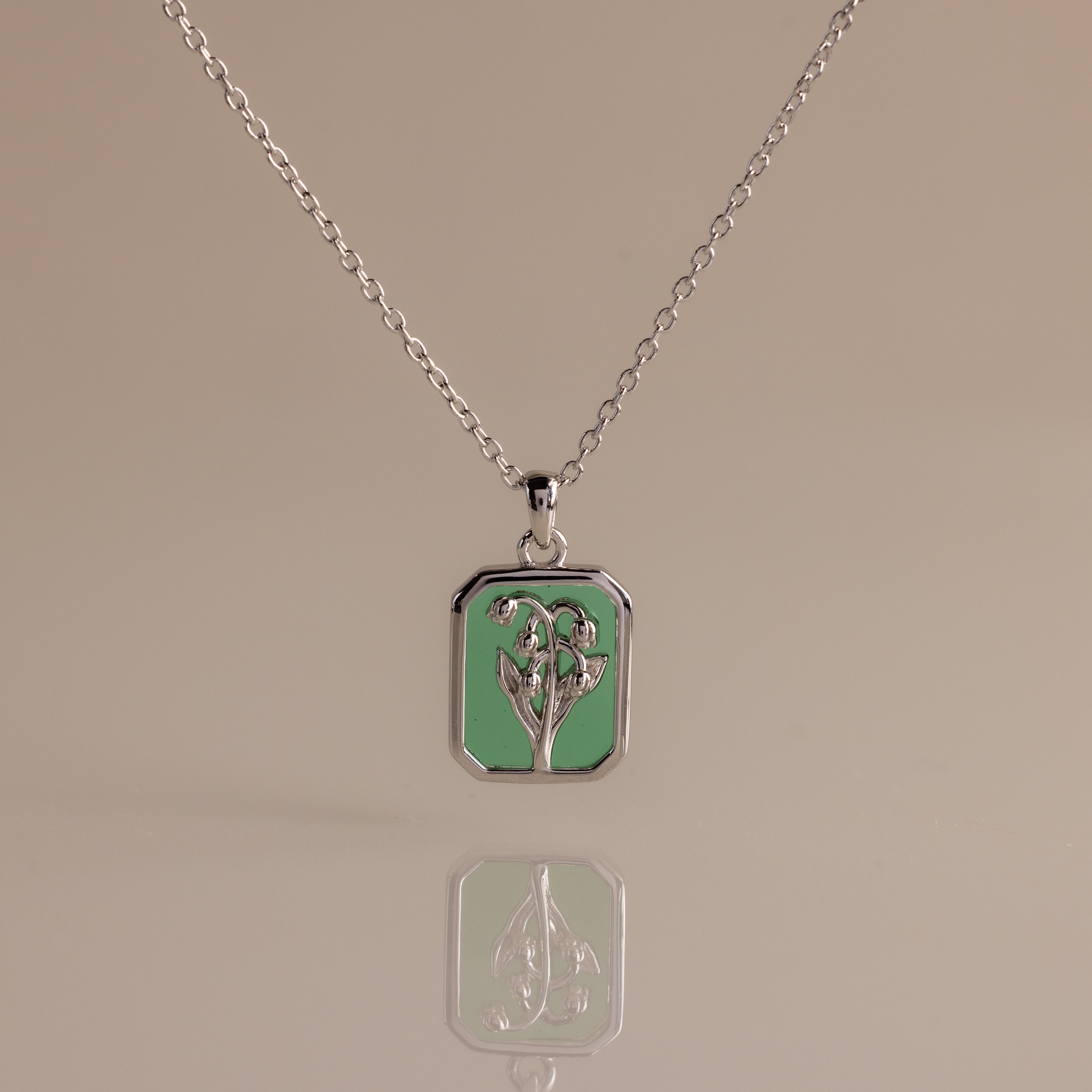 Silver necklace with a rectangular green emerald birth flower charm displayed on a reflective surface—I'm sorry, but there is no product description provided for further details.