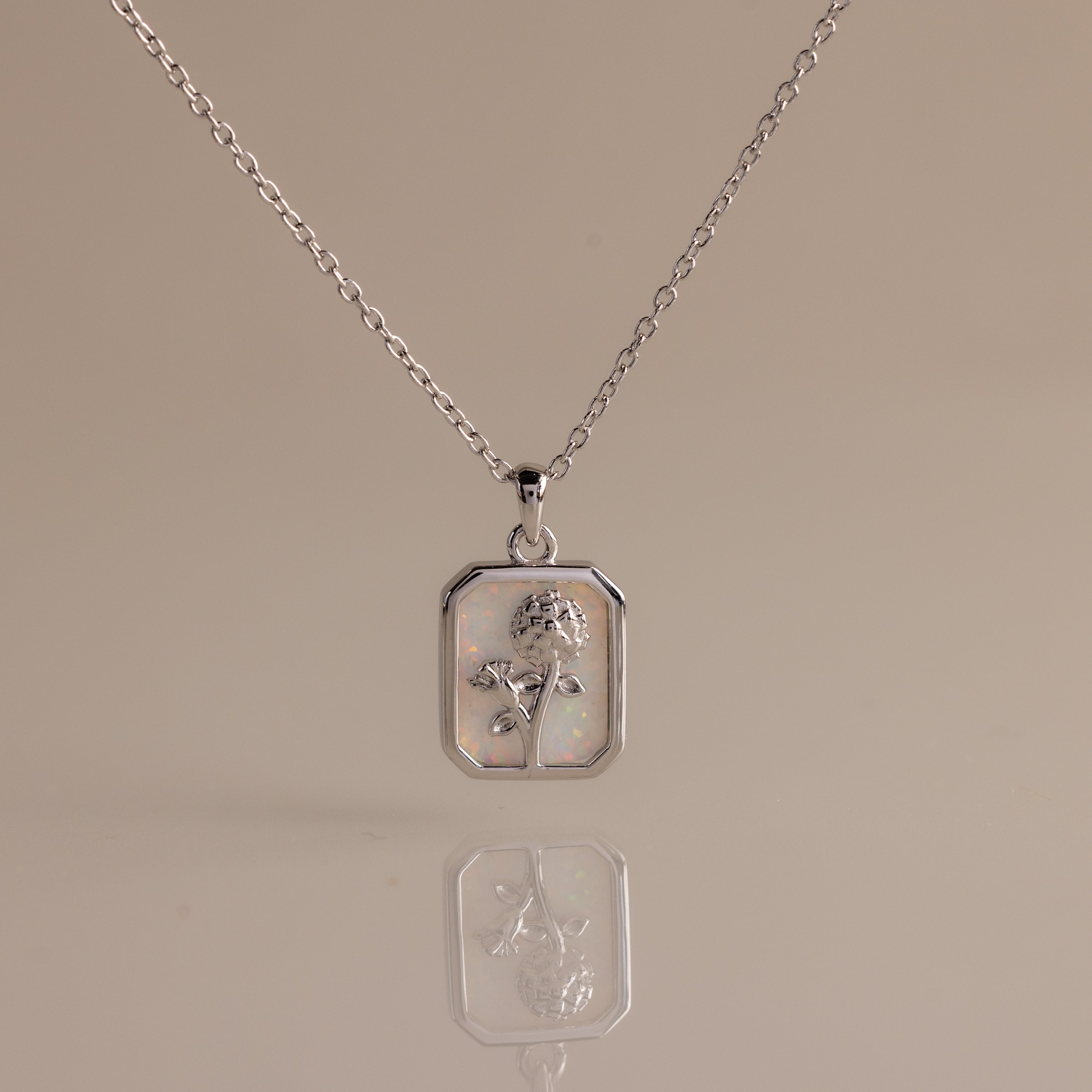 Opal Birth Flower Charm Necklace: A silver necklace with a rectangular pendant showcasing a delicate birth flower design on a light, reflective background—ideal for adding elegance to any outfit.