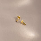 Two 18k gold Flat Back Posts lying on a matte surface