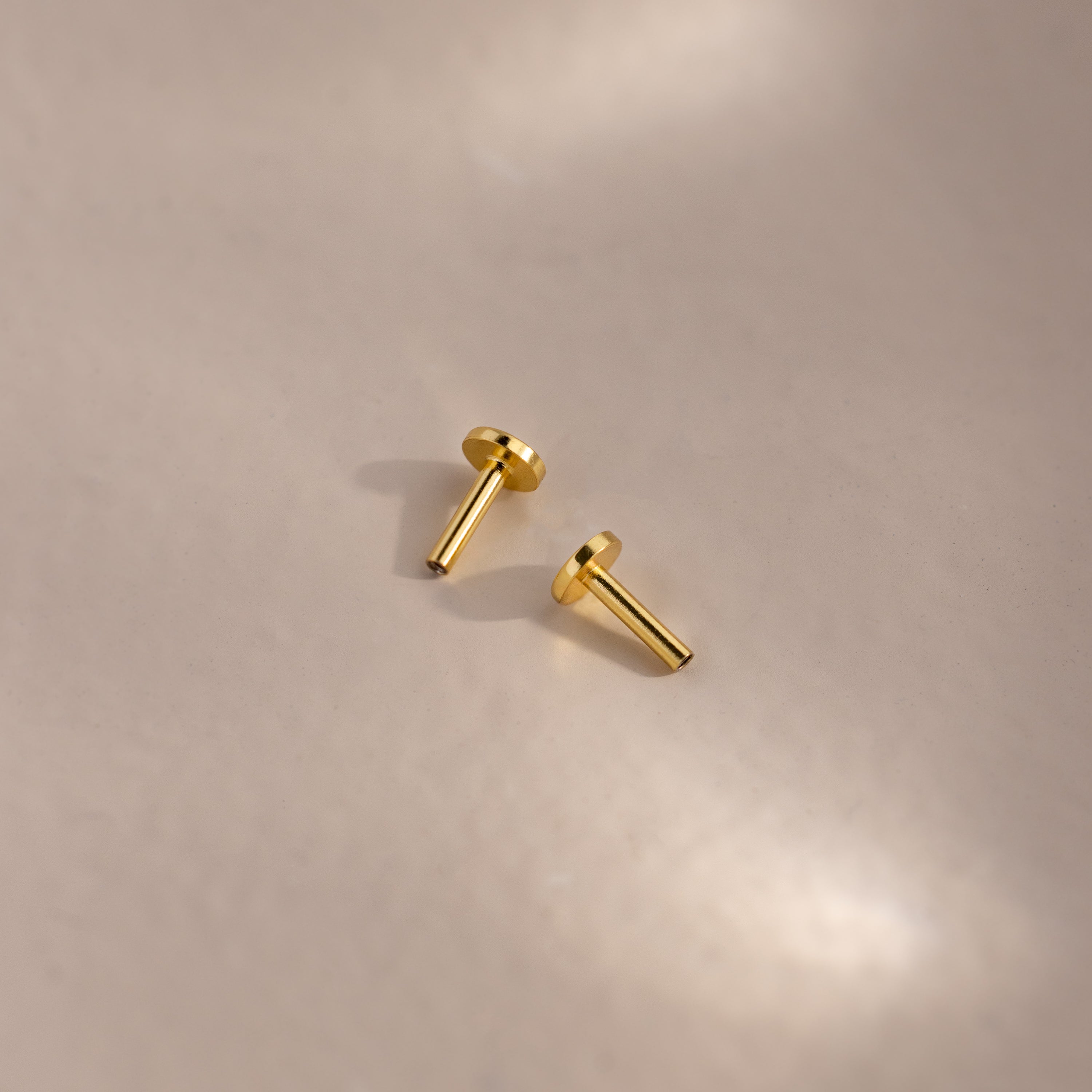 Two 18k gold Flat Back Posts lying on a matte surface