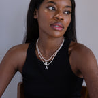 A woman in a black tank top wears the Newsletter Pearl Initial Necklace in Sterling Silver, featuring customizable letter charms for a minimalist jewelry look as she gazes to the side.