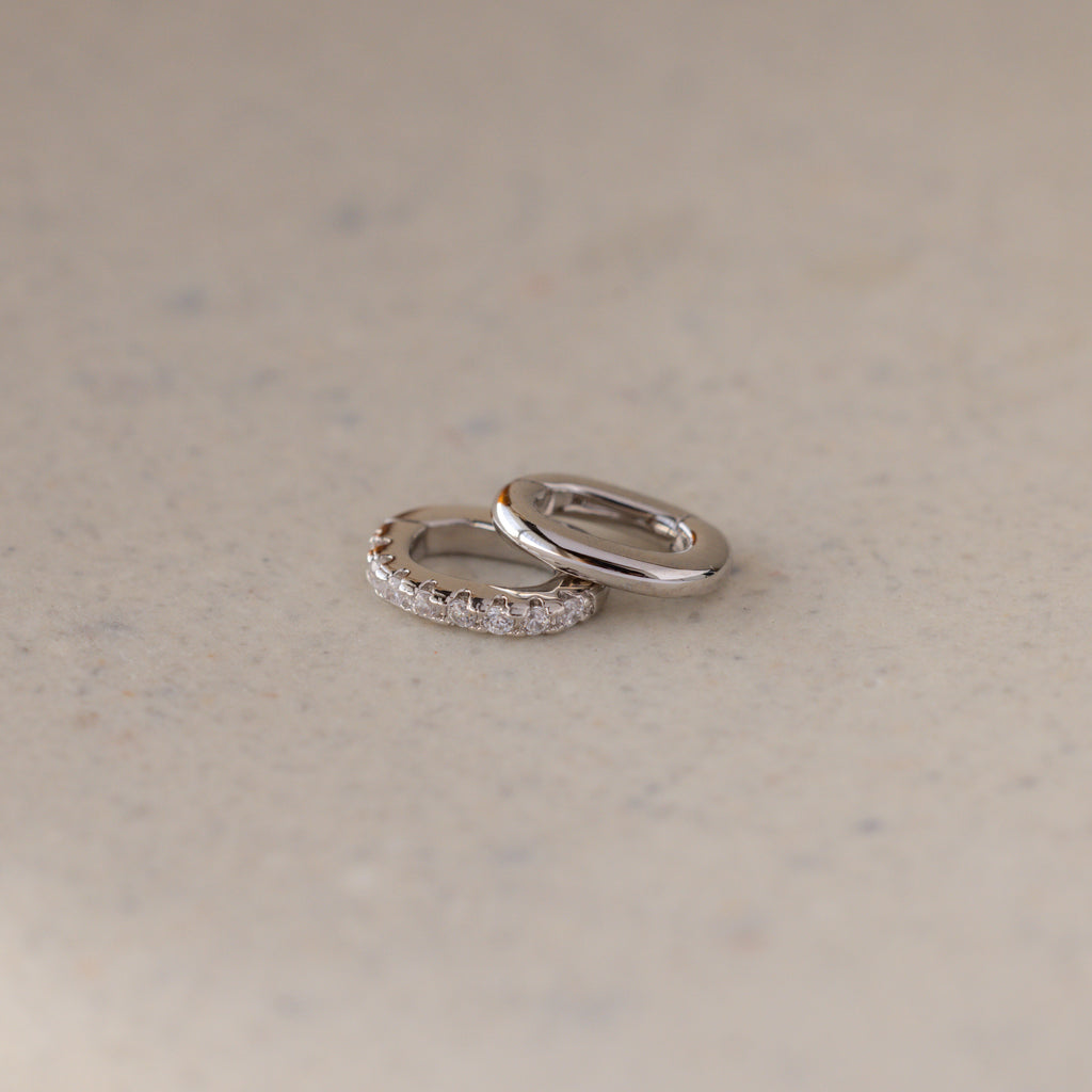 The Multipurpose Pave Ring Lock Set in White Gold features two rings—one plain, one with small diamonds—resting on a light beige surface, offering elegant, customizable jewelry for refined tastes.