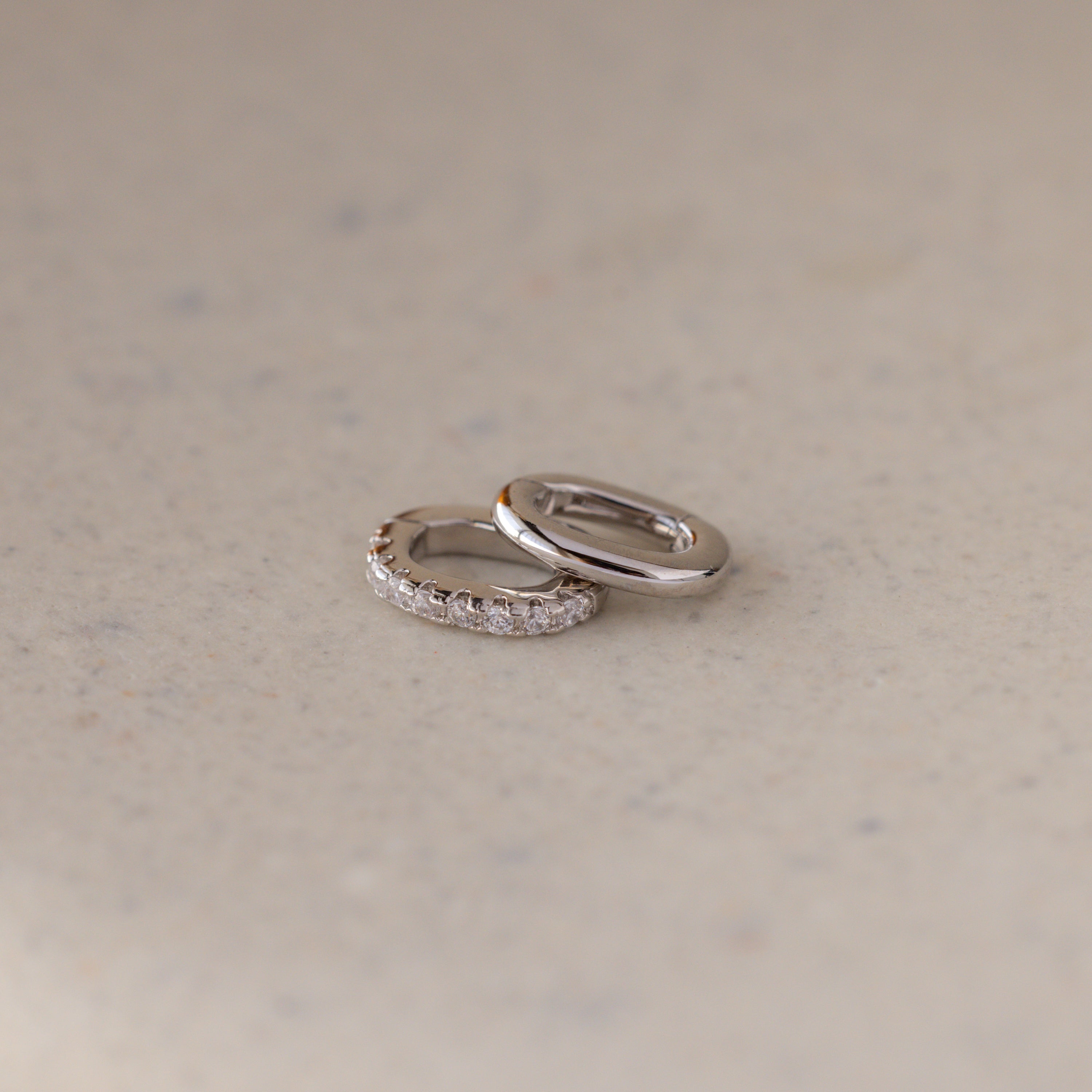 The Multipurpose Pave Ring Lock Set in White Gold features two rings—one plain, one with small diamonds—resting on a light beige surface, offering elegant, customizable jewelry for refined tastes.