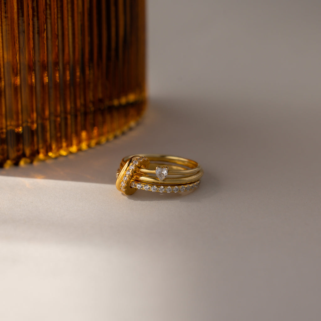 Multipurpose Pave Ring Lock Set in 18K Gold, featuring a pavé-detailed clasp, stacked beside a ribbed amber glass object on a neutral surface—an ideal accent for personalized jewelry styling.