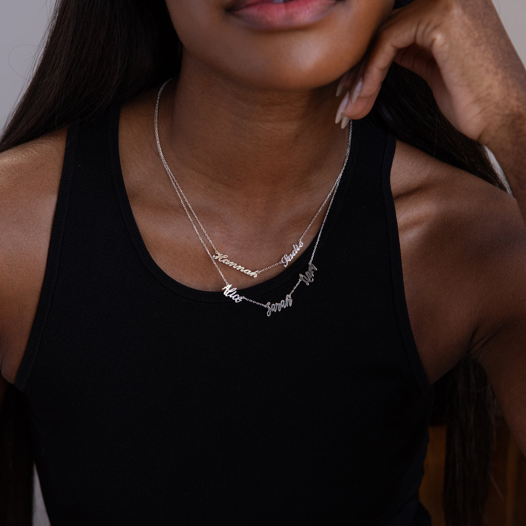 Woman in a black tank top wears the Carrie Multiple Name Necklace in Sterling Silver, featuring two personalized silver name pendants, shown from the shoulders up.