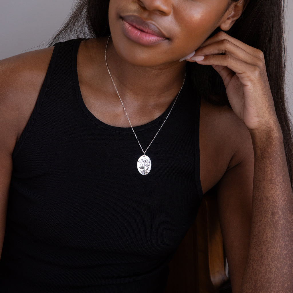 Woman in a black sleeveless top wears the Oval Flower Necklace, a silver pendant with a tree design—ideal for pairing with unique floral jewelry or an elegant birth flower necklace.