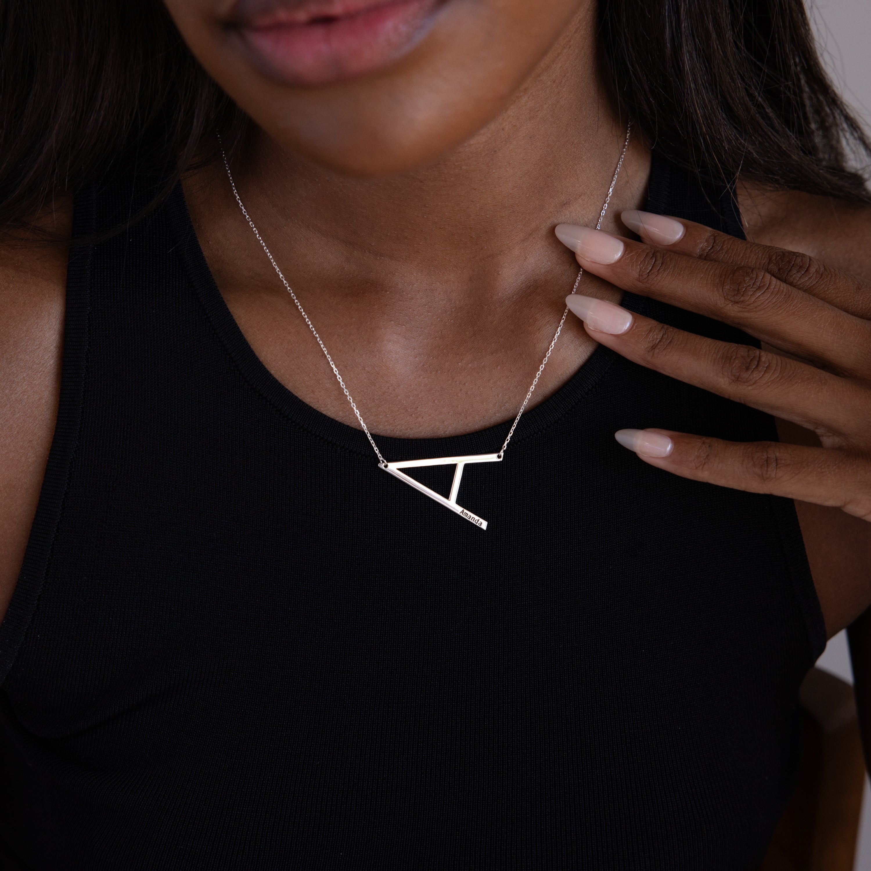 Woman wearing a black top showcases the Large Sideways Initial Necklace in Sterling Silver, gently touching its bold geometric chain with her manicured hand.