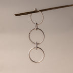 Three silver rings, one with pavé details, are suspended from a brown twig against a neutral background—perfect for customizing your own Multipurpose Pave Ring Lock Set.
