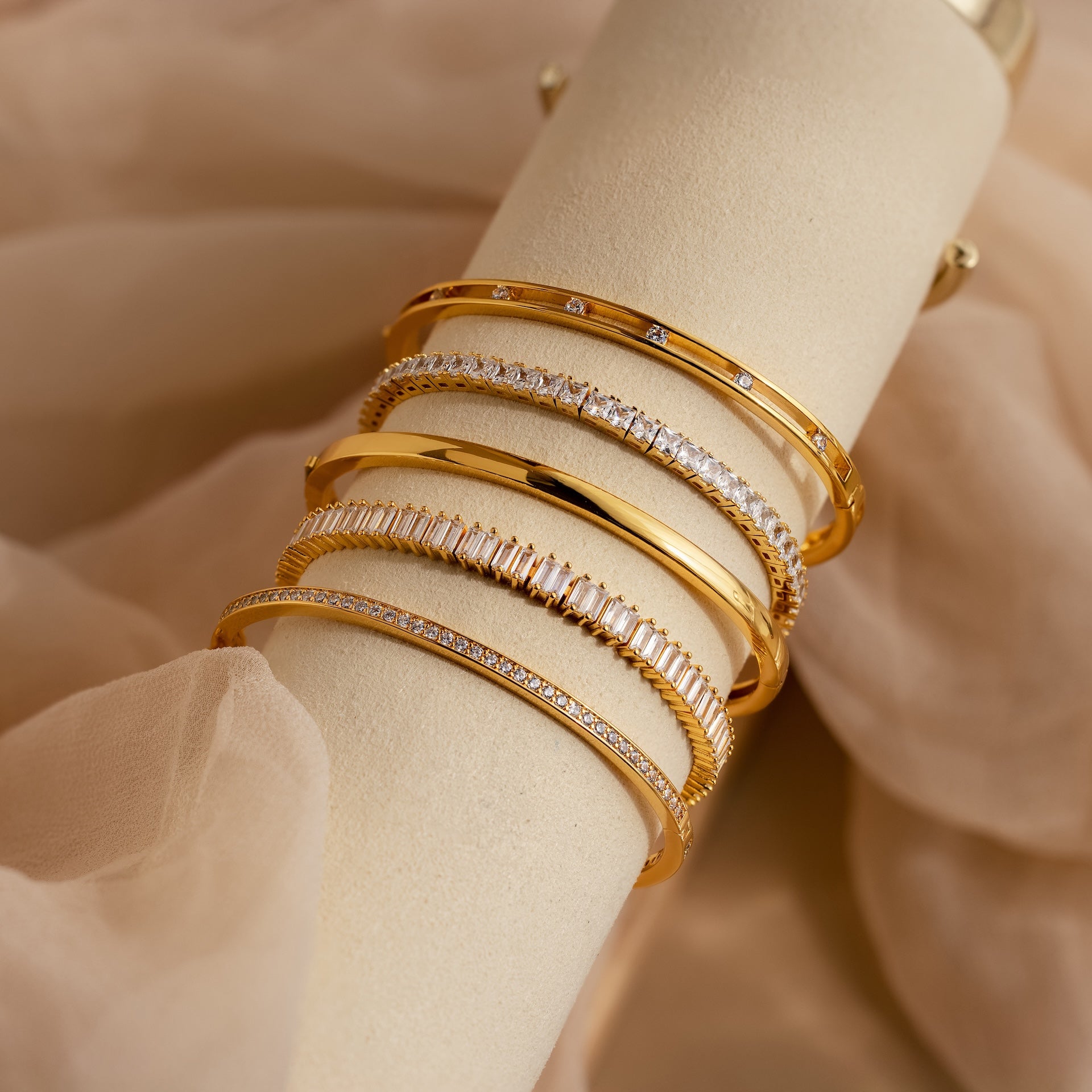 A Princess Diamond Tennis Bracelet, featuring sparkling princess-cut diamonds, displayed elegantly on a cream-colored stand with a soft beige fabric background.