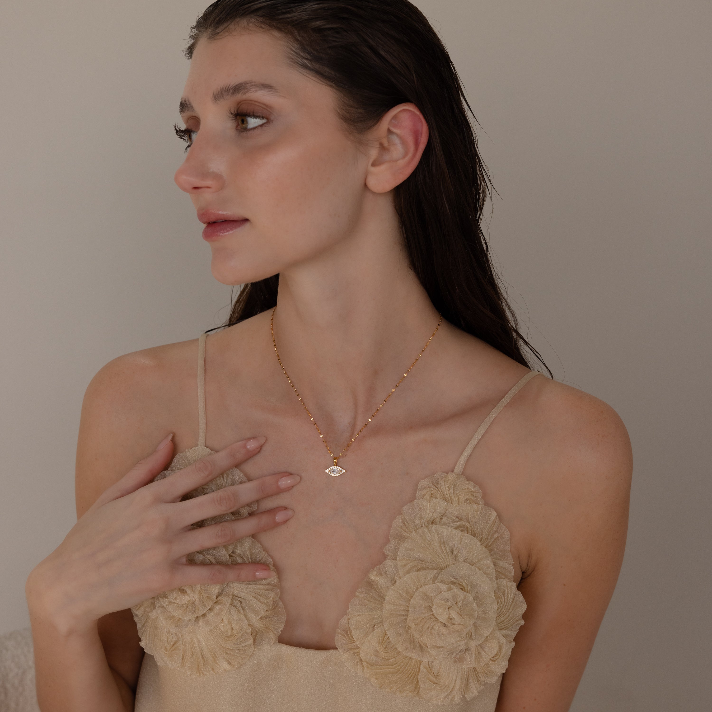 Model poses while wearing gold mirror chain with dangling pave evil eye charm