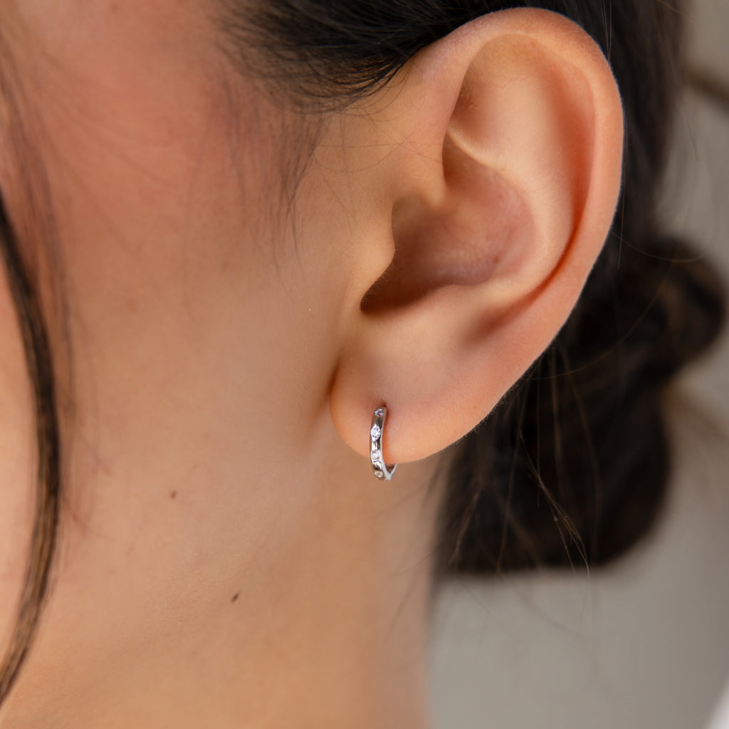 Close-up of an ear wearing Mini Diamond Sprinkle Huggies in Silver—petite, shimmering huggie hoops that catch the light with every movement.