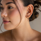 Woman with neatly styled hair wears three small gold huggie hoops, including Mini Diamond Sprinkle Huggies that add a subtle sparkle, in her left ear as she looks to the side.