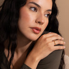 A woman with long dark hair wears the Minimal Stacking Ring in 18K Gold, looking thoughtfully to the side against a beige background.