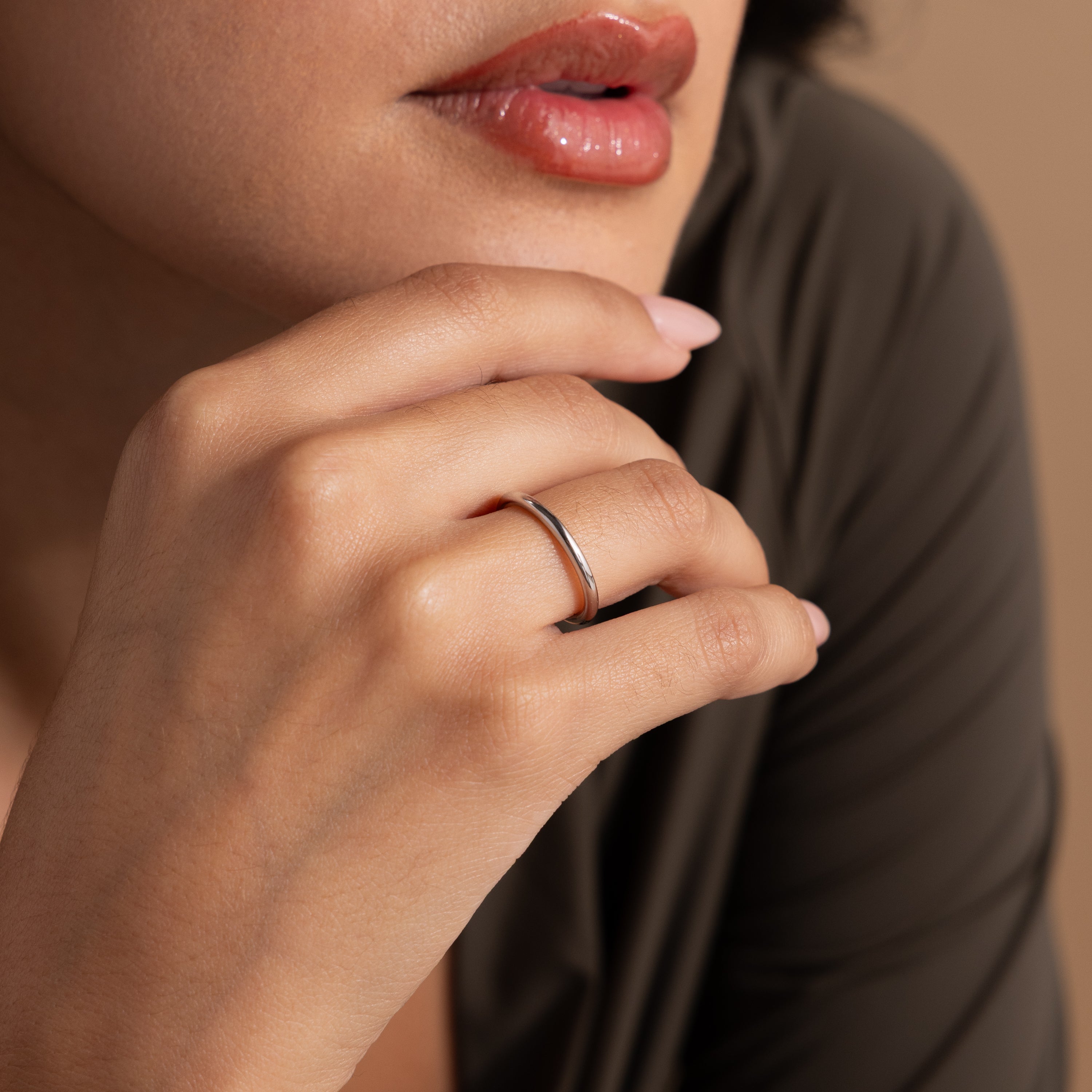 A woman with glossy lips touches her chin, showcasing the Minimal Stacking Ring in Silver on her finger.