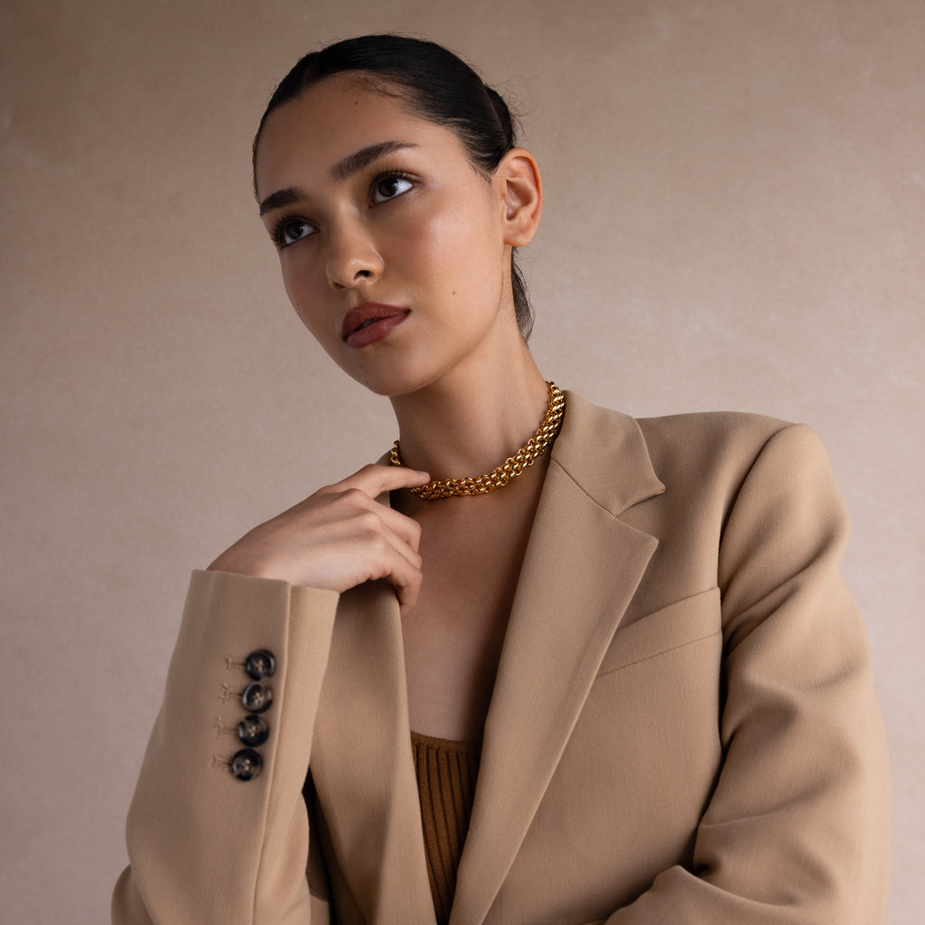 Woman in a tan blazer and gold necklace poses against a neutral background, offering perfect inspiration for the Corporate Gift Box—an ideal choice for curated jewelry or personalized business gifts.