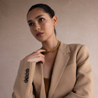 Woman in a tan blazer and gold necklace poses against a neutral background, offering perfect inspiration for the Corporate Gift Box—an ideal choice for curated jewelry or personalized business gifts.