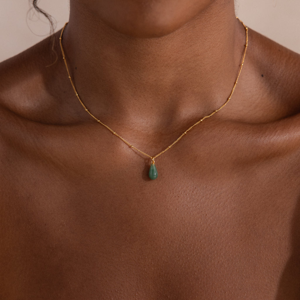 Close-up of model wearing a minimal gold satellite chain necklace featuring a single green jade teardrop gemstone pendant.