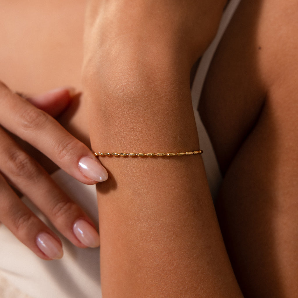 The Oval Beaded Bracelet in 18K Gold graces the wrist, with manicured fingers gently touching the arm—a refined piece of modern jewelry.