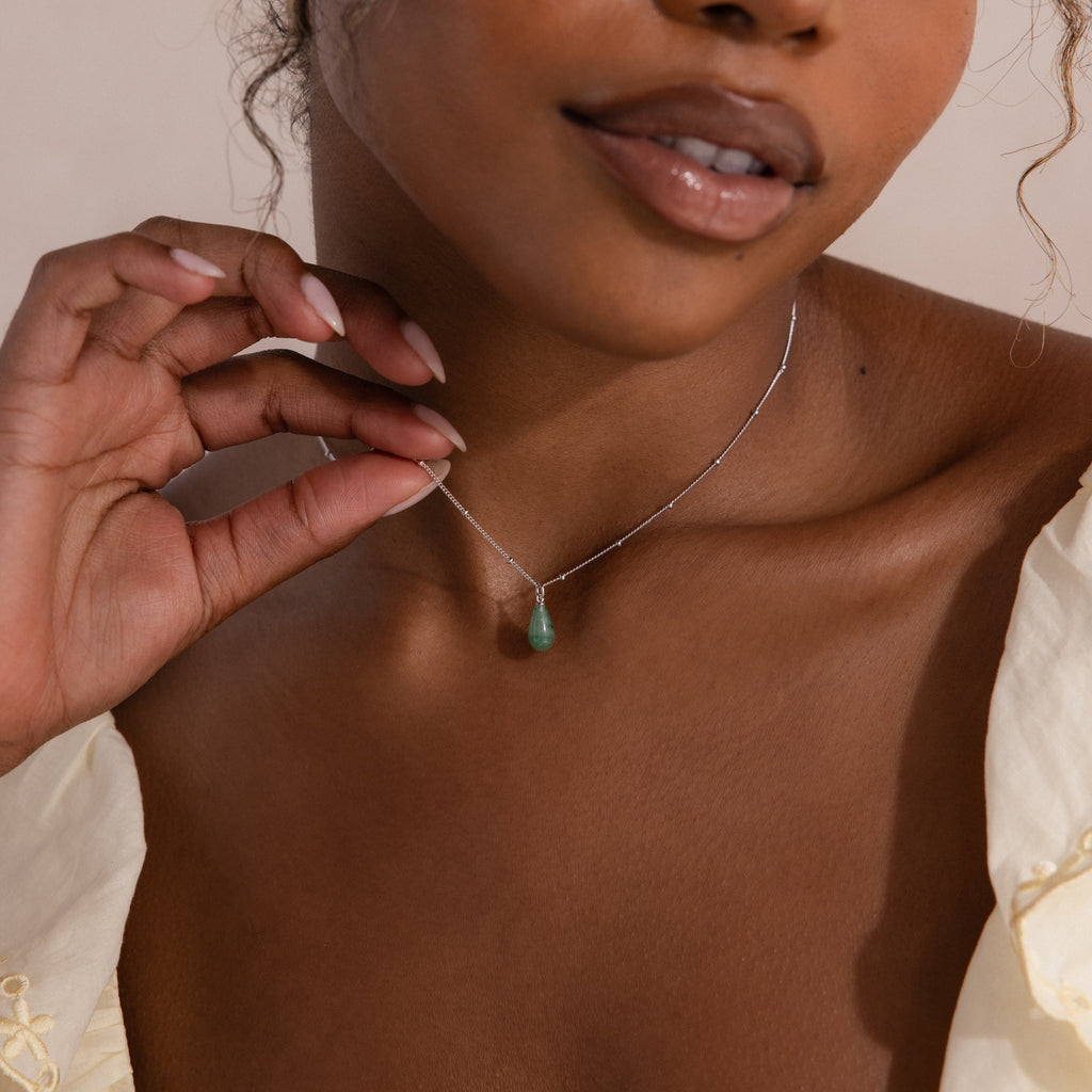 Model wearing a silver satellite chain necklace featuring a single green jade teardrop gemstone pendant.