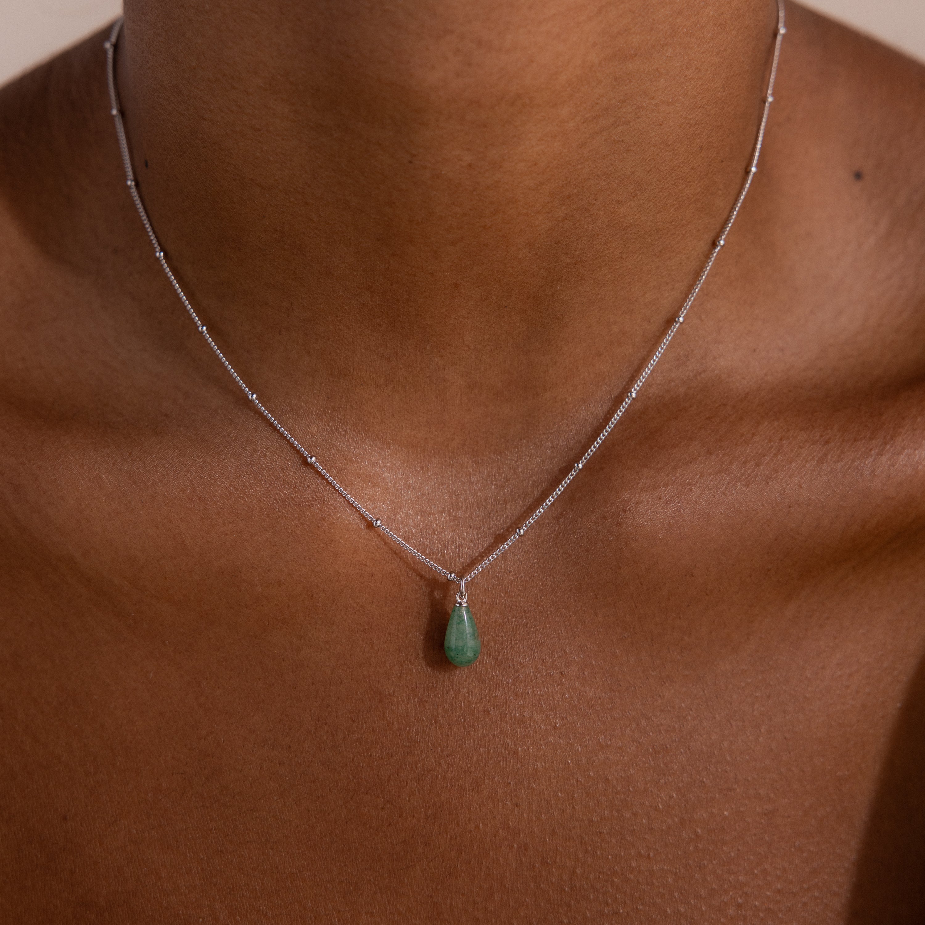 Model wearing a silver satellite chain necklace featuring a single green jade teardrop gemstone pendant.