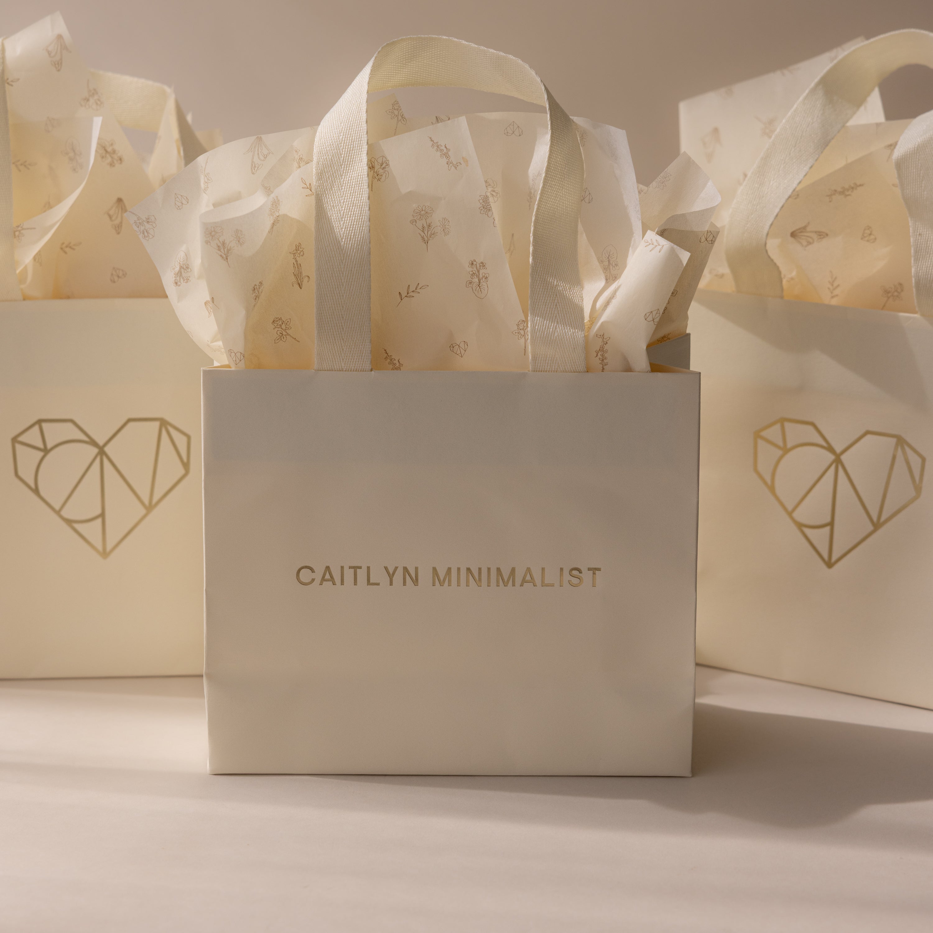 Add the Gift Bag Add-On—featuring CAITLYN MINIMALIST branding, a geometric heart design, and floral tissue paper—for an elegant finishing touch to your gift wrapping.