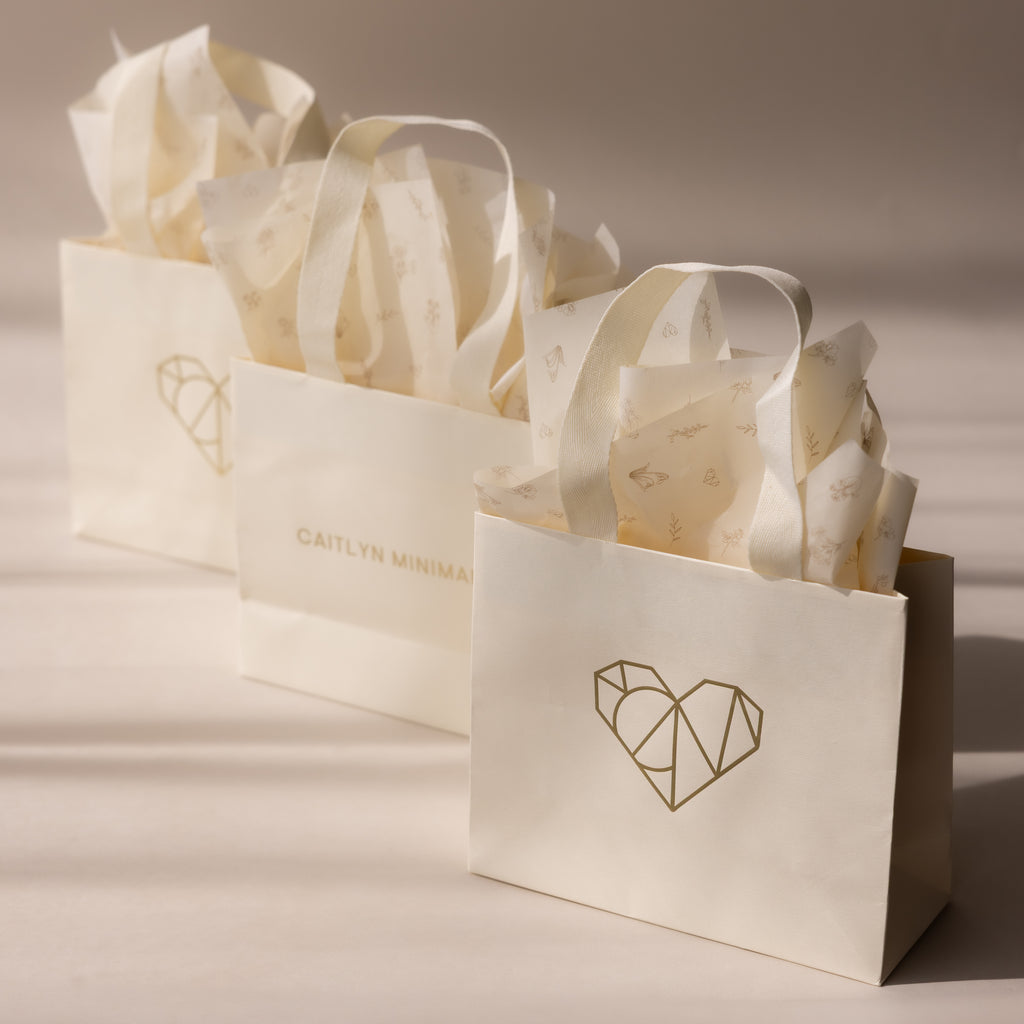 Three elegant cream-colored Gift Wrap Add-On bags feature white tissue paper and minimalist gold designs, providing a stylish finishing touch for any occasion.