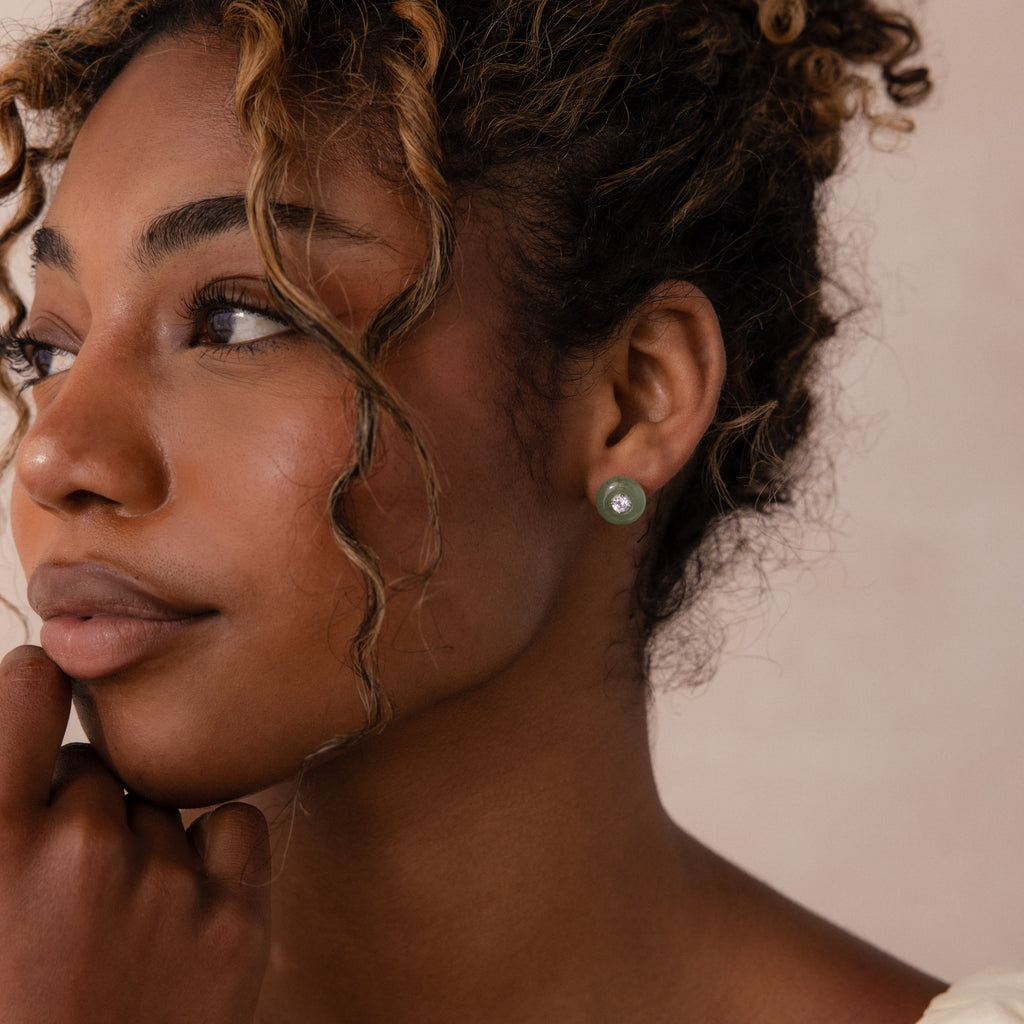 Model wearing a round green jade stud earring with a centered CZ diamond accent and silver bezel.