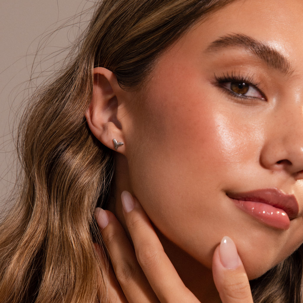 Close-up of a woman with wavy hair wearing a small Shark Tooth Flatback Stud earring, touching her neck gently—a subtle beach accessory for effortless style.