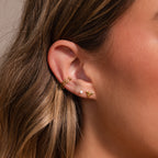 Close-up of a womans ear with three gold earrings—a double cuff, a small stud, and a bird-shaped stud—styled as chic beach accessories or perfectly paired with our Shark Tooth Flatback Studs.