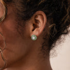 Model wearing a round green jade stud earring with a centered CZ diamond accent and silver bezel.