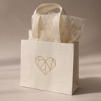 The Gift Bag Add-On features a cream hue with a geometric heart design and patterned tissue paper—an elegant way to wrap gifts and add a special touch.