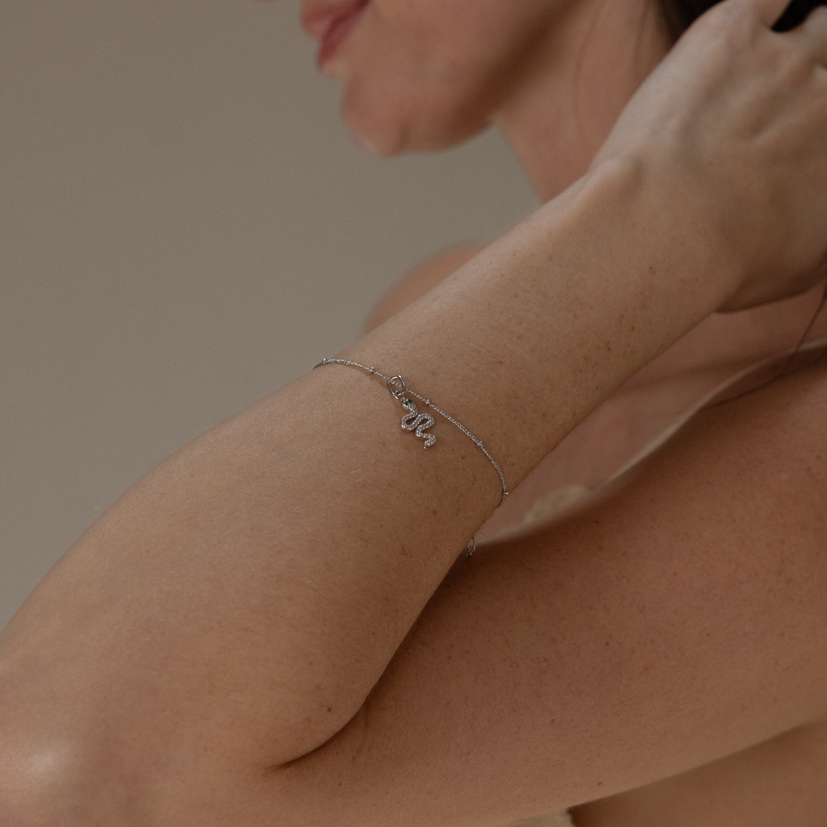 Model wears a silver satellite bracelet with dangling diamond snake charm