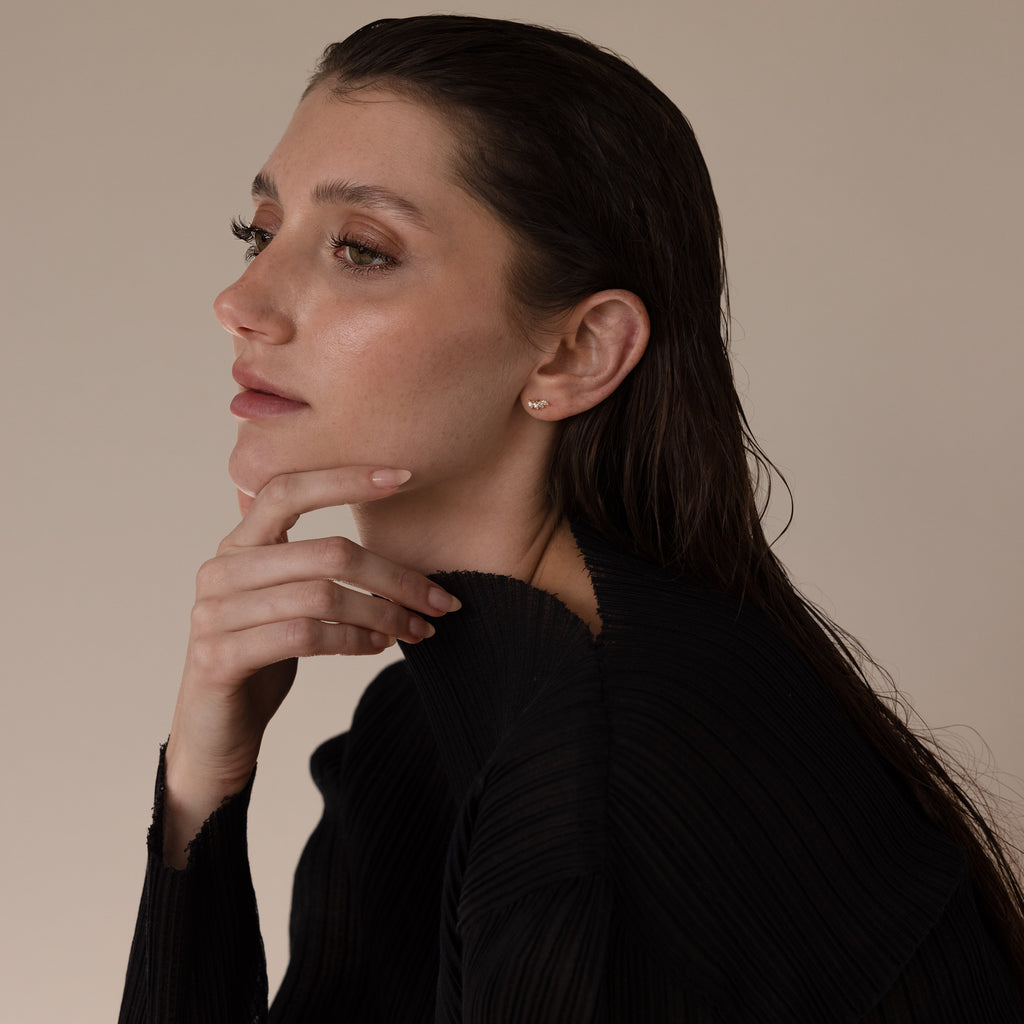 Woman with wet, dark hair in a black top gazes thoughtfully to the side, her look elegantly accented by Marquise Diamond Climbers in 18K Gold.