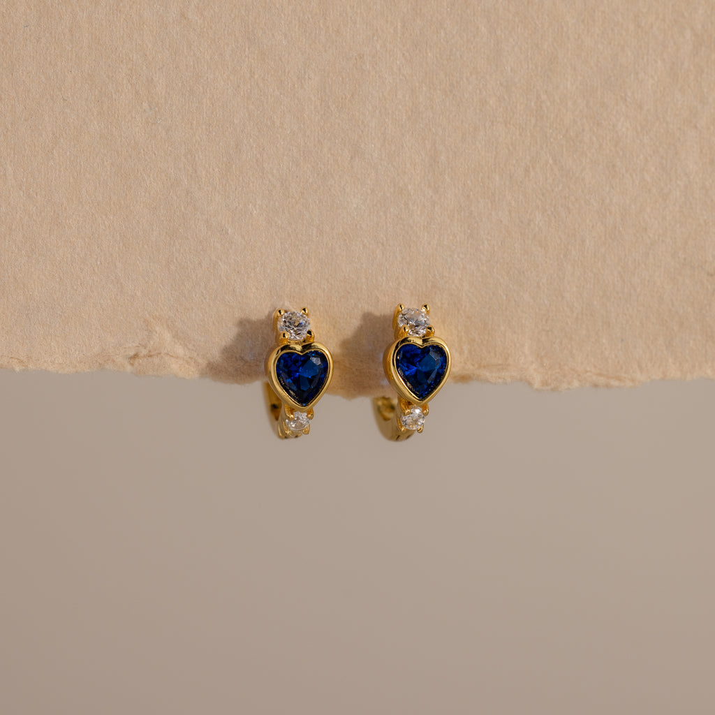 Sapphire Heart Hoops—gold earrings with blue heart-shaped stones and small clear gems—are perfect birthstone earrings to add elegance to any look.