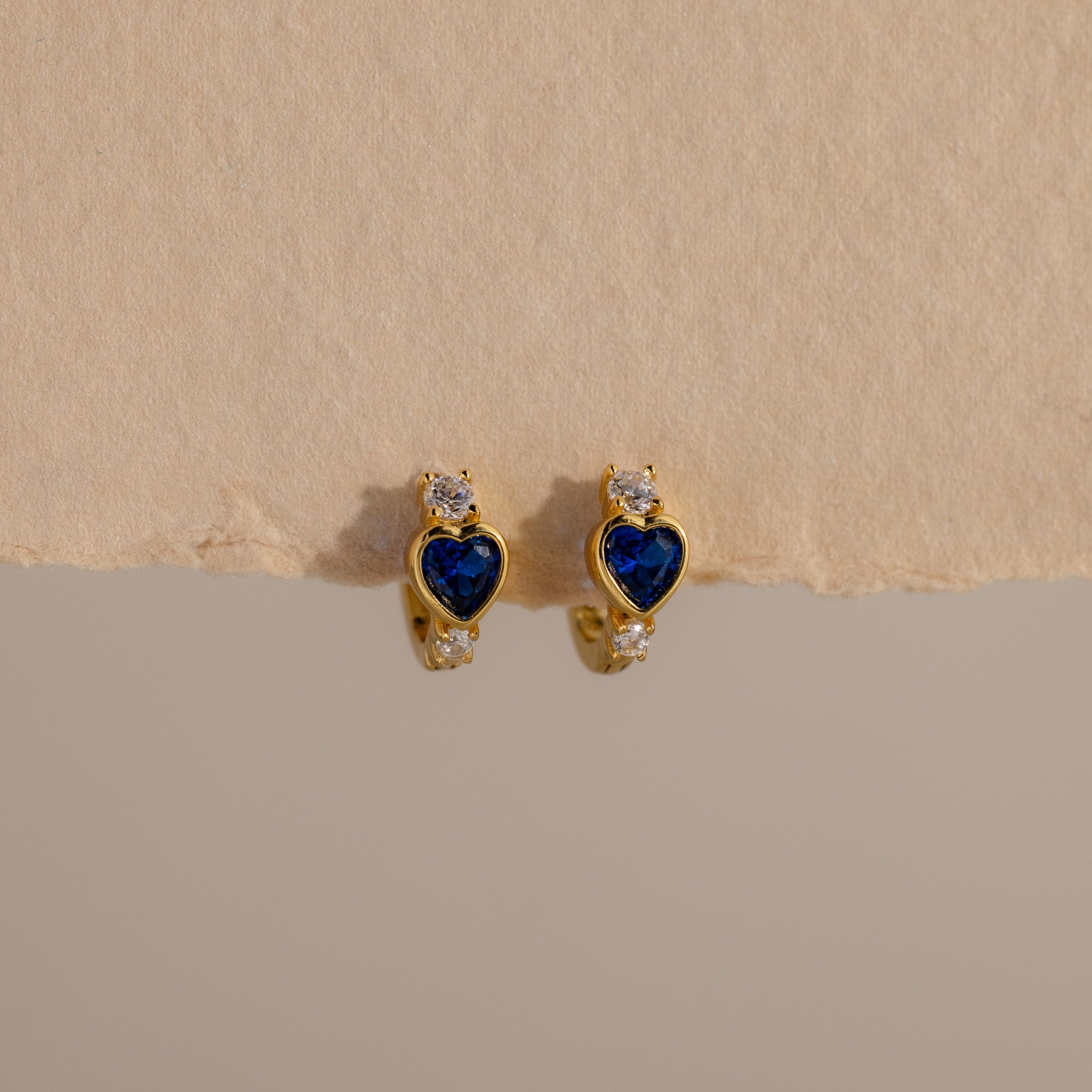 Sapphire Heart Hoops—gold earrings with blue heart-shaped stones and small clear gems—are perfect birthstone earrings to add elegance to any look.
